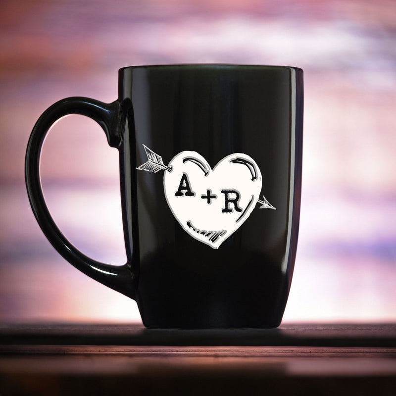 Black ceramic mug with engraved heart and arrow design featuring sample initials "A+R