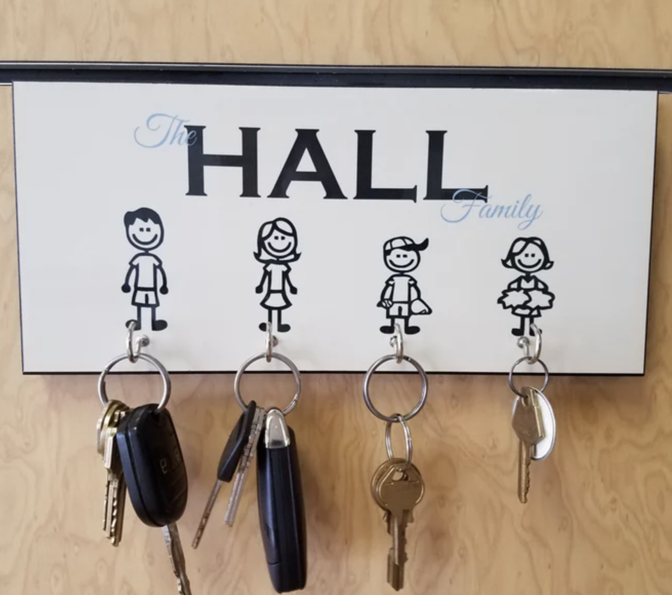White key holder with "The Hall Family" text and four stick figures representing family members, each with a metal hook below for hanging keys